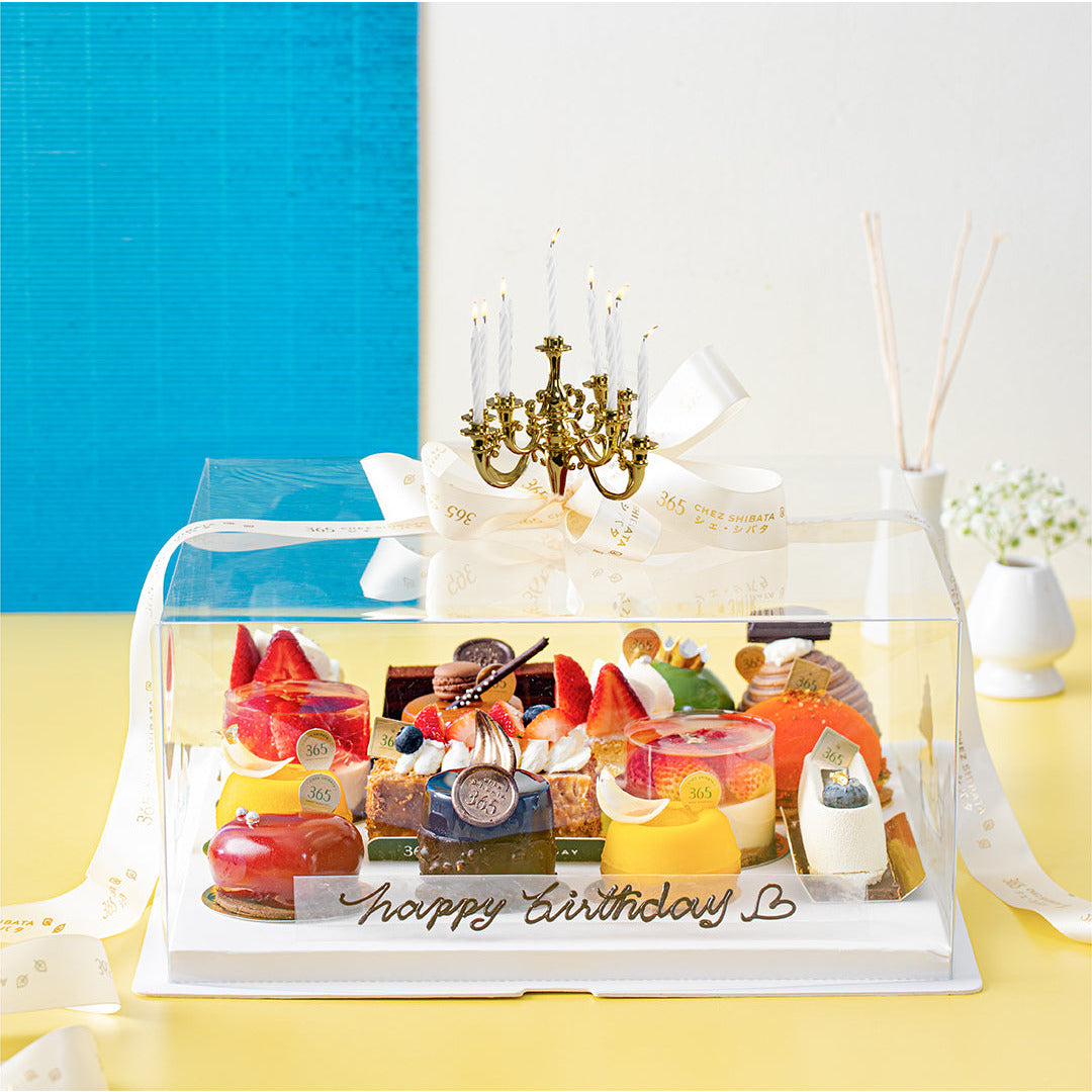 Happy Birthday” บนฐานกล่อง พร้อมเชิงเทียนสไตล์หรูหราสำหรับปักเทียนวันเกิด เพิ่มบรรยากาศพิเศษ พื้นหลังสีเหลืองและฟ้า เสริมความสดใสและน่าประทับใจ