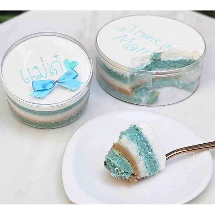 Blue and white layered cake in a transparent container with a slice on a plate.
