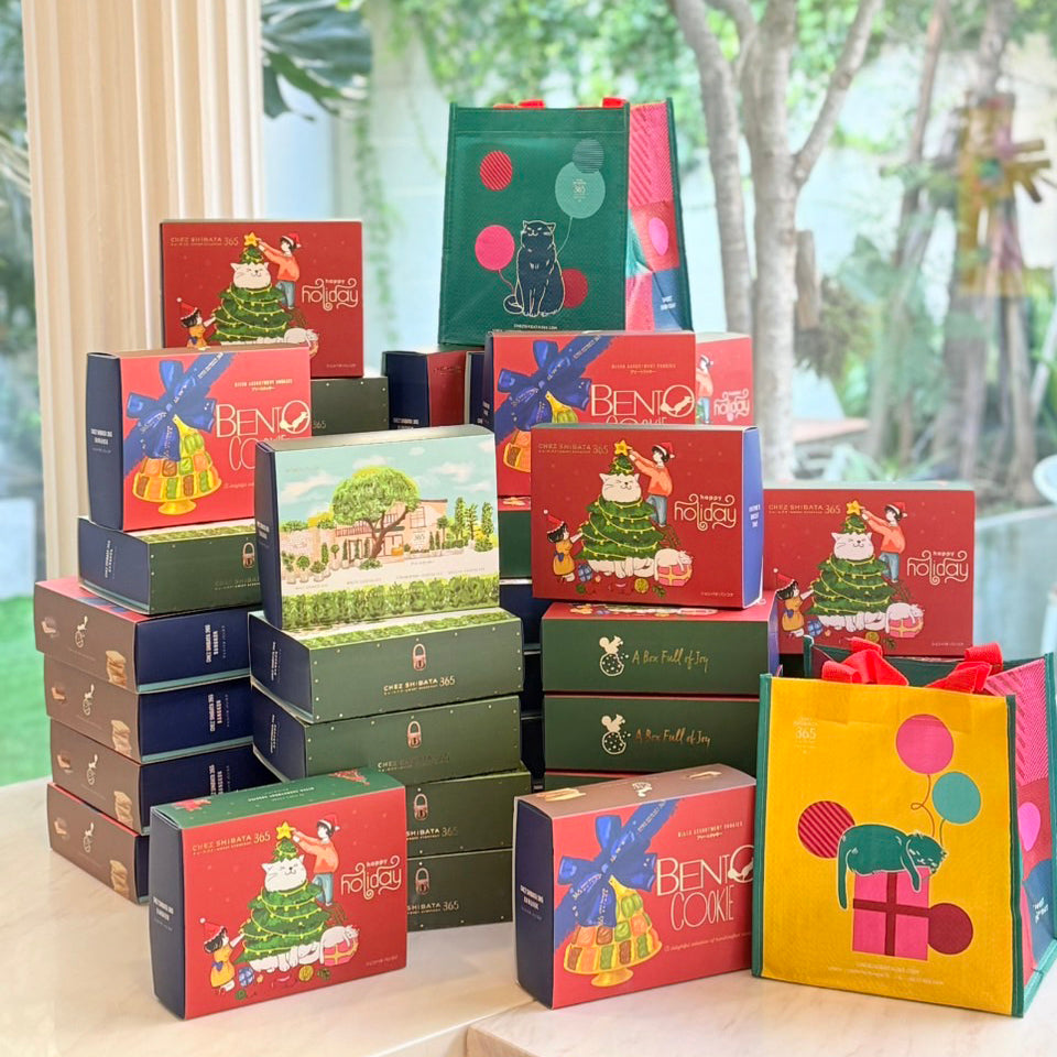 Collection of colorful Beno cake boxes on a table with a blurred outdoor Chez Shibata365