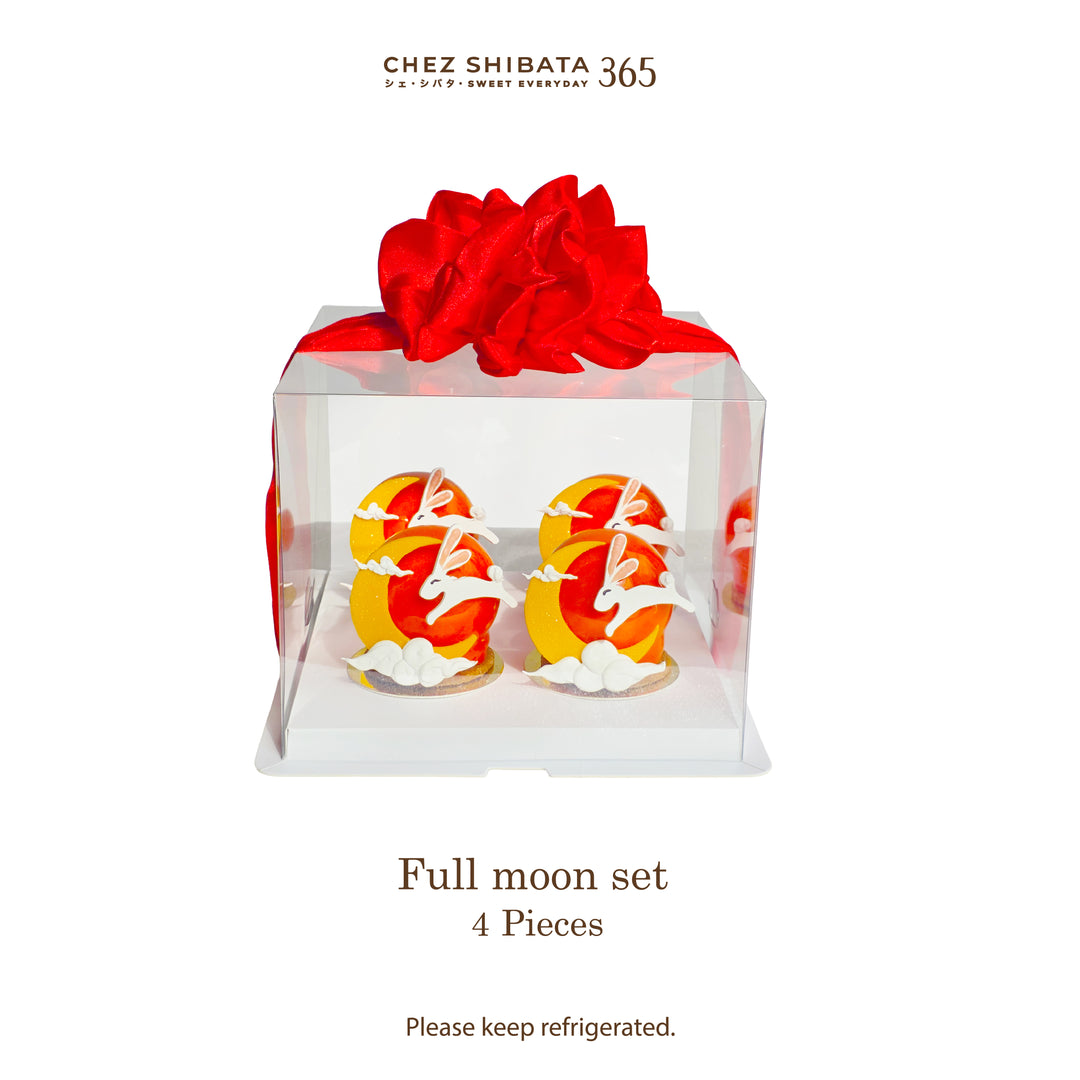 A clear square bakery box with a large red ribbon bow on top, containing two decorated pastries shaped like full moons with white cloud accents. The image includes the brand name Chez Shibata 365 at the top and text reading &