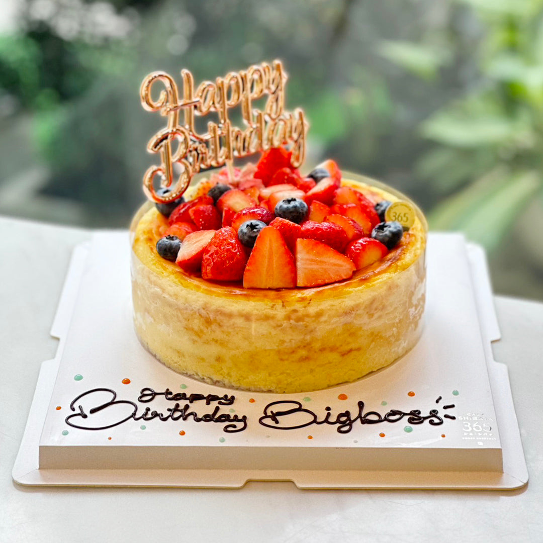 New York Cheesecake ตกแต่งด้วยสตรอว์เบอร์รี่และบลูเบอร์รี่สด พร้อมป้าย “Happy Birthday” สีโรสโกลด์ วางบนถาดสีขาวที่มีข้อความอวยพรเขียนด้วยดาร์กช็อกโกแลตเกลซ บรรจุในกล่องของขวัญใสพร้อมโบว์ที่สามารถเลือกสีได้ เหมาะสำหรับเป็นของขวัญวันเกิดหรือโอกาสพิเศษ