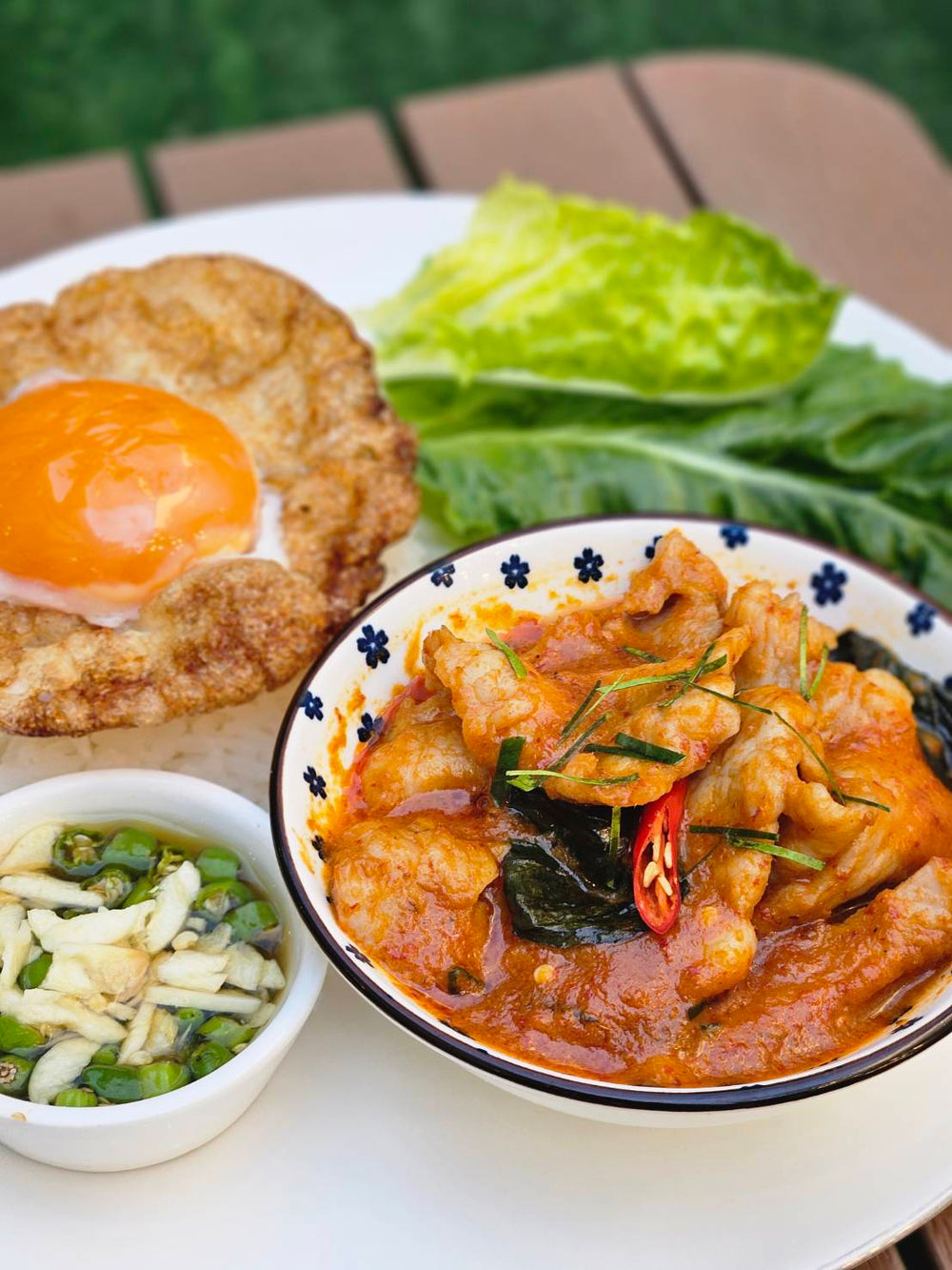 Thai panaeng curry with pork served with steamed jasmine rice, crispy fried egg, fresh greens, and chili fish sauce