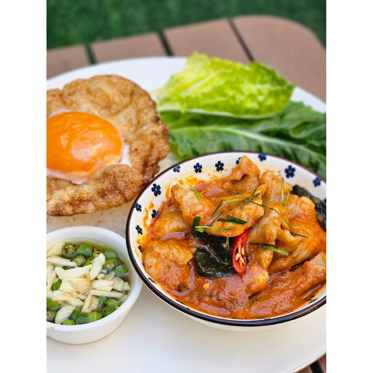 Thai panaeng curry with pork served with steamed jasmine rice, crispy fried egg, fresh greens, and chili fish sauce